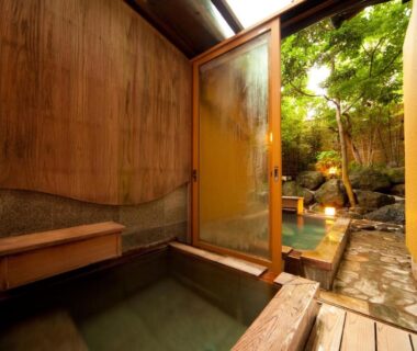 Indoor wooden bath opening to outdoor stone onsen and garden at Kappo Ryokan Kannawa Bettei Oita