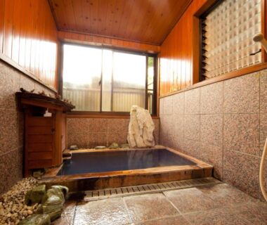 Indoor tiled soaking tub with wooden ceiling and stone feature at Kappo Ryokan Kannawa Bettei in Ōita
