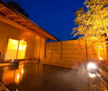 Nighttime outdoor onsen courtyard with wooden deck and lit shoji interior at Kappo Ryokan Kannawa Bettei, Ōita