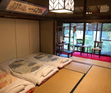 Tatami room with futons, sliding doors, low table and chairs overlooking garden at Kappo Ryokan Uoichi Shizuoka