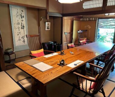 Long wooden table on tatami with low chairs, shoji screens and calligraphy scroll overlooking garden at Kappo Ryokan Uoichi