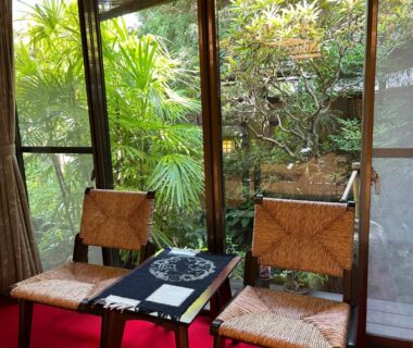 Two woven chairs and low table beside large windows overlooking a lush courtyard garden at Kappo Ryokan Uoichi, Shizuoka