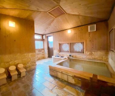 Indoor wooden bathing area with tiled floor, soaking pools and wash stools at Kappo Ryokan Yumesaki Oita