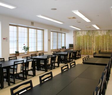Spacious ryokan dining room with rows of black tables, shoji windows and bamboo screen