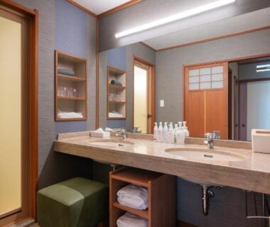 Double sink vanity with wooden counter, mirror, stool and neatly folded towels in Kashikojima Hojoen bathroom, Mie