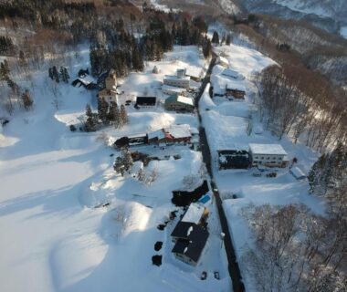 Aerial view of snow-covered ryokan buildings and road at Kashiwaya Gassan in Yamagata mountains