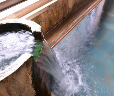 Indoor onsen with stone spout pouring water into wooden-edged bath at Kashiwaya Ryokan, Fukushima