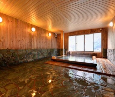 Warm wooden indoor onsen with stone floor and sunken bath at Kashiwaya Ryokan in Fukushima