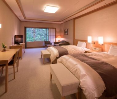 Twin guest room with two beds, desk, seating, and large window overlooking greenery at Kashoen in Iwate, Tōhoku