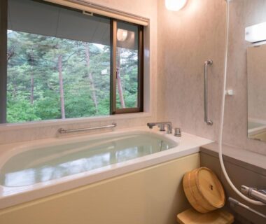 Bathtub and shower with wooden stool, window framing green forest at Kashoen, Iwate Tōhoku