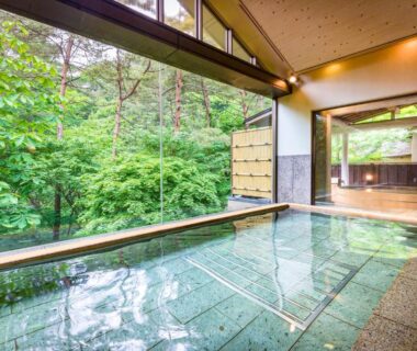Glass-walled indoor onsen overlooking lush forest, tiled bath and wooden decking at Kashoen Iwate