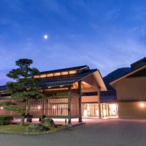 Dusk-lit Kashoen entrance with traditional wooden architecture, illuminated interior and courtyard under a moonlit sky in Iwate, Tōhoku