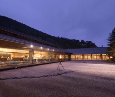 Lit courtyard with raked gravel and glass-fronted ryokan at dusk, Kashoen in Iwate Tohoku