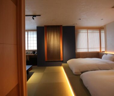Room with tatami flooring, two futon beds, shoji screens, soft ambient lighting, decorative wall hanging and wooden accents