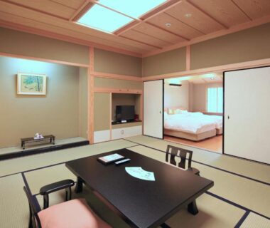 Spacious tatami room with low table, seating cushions, sliding shoji doors and adjoining futon sleeping area at Kasuga Hotel, Nara
