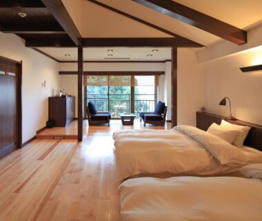 Spacious twin room with wooden floors, exposed beams and seating by large window overlooking greenery at Kasuga Hotel Nara