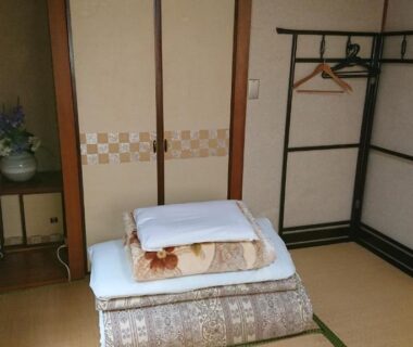 Traditional tatami room with folded futon, sliding doors and wooden clothes rack at Kasuga Ryokan in Hiroshima