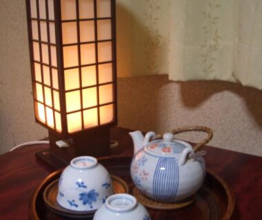 Ceramic teapot and two cups on wooden tray beside shoji-style lamp in ryokan guest room