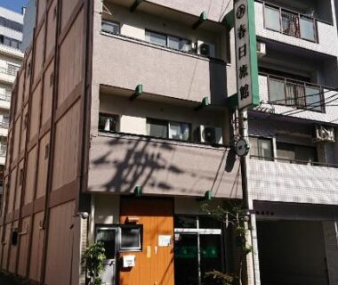 Narrow multi-story ryokan exterior with street-level entrance and vertical sign in Hiroshima