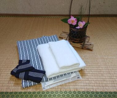 Folded towels and striped yukata on tatami mat with small floral arrangement at Kasuga Ryokan Hiroshima