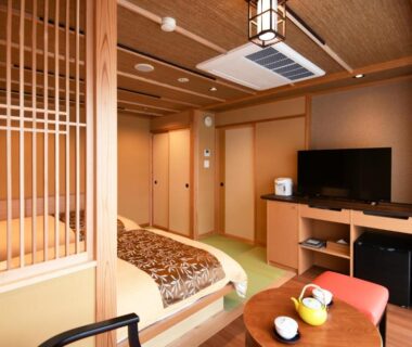 Tatami room with low bed, wooden lattice divider, TV and small tea set at Kasuitei Ooya, Yamanashi