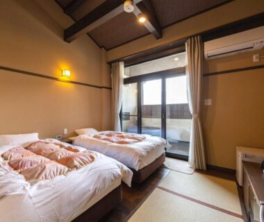 Tatami-floored twin room with low beds and balcony door at Katsuragi Onsen Happuu No Yu, Wakayama