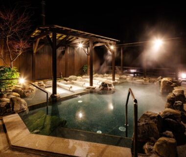 Outdoor onsen bath at night with steam, lantern lighting and wooden pergola at Katsuragi Onsen Happuu No Yu Wakayama
