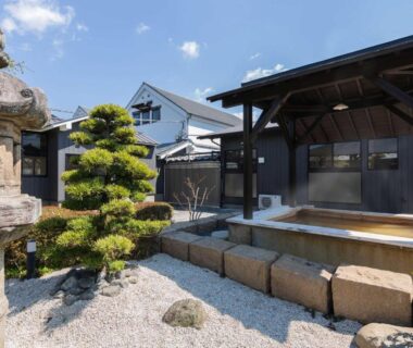 Wooden onsen tub beside stone lantern and pruned pine in garden at Katsuragi Onsen Happuu No Yu, Wakayama