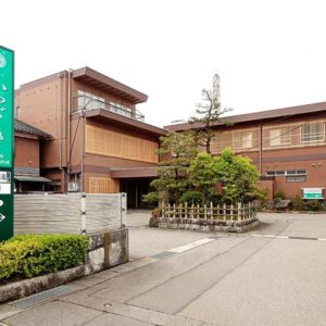 Traditional multi-story wooden ryokan exterior with green signboard and small courtyard at Katsuzakikan, Ishikawa