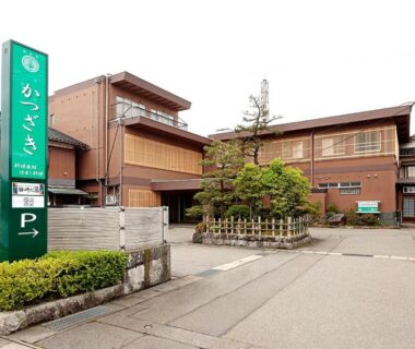 Traditional multi-story wooden ryokan exterior with green signboard and small courtyard at Katsuzakikan, Ishikawa