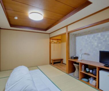 Simple tatami room with folded futon, low TV shelf and wooden ceiling at Katsuzakikan in Ishikawa, Chūbu