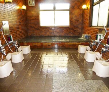 Brick-walled indoor communal bath with stools, hand showers and tiled soaking tub at Kawaguchiko Lakeside Hotel, Yamanashi
