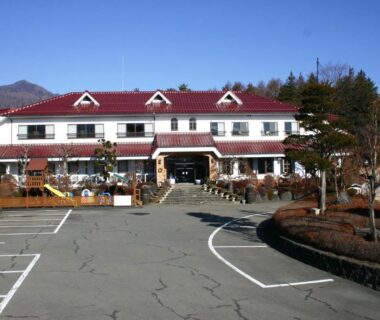 Hotel exterior and parking lot at Kawaguchiko Lakeside Hotel with mountain backdrop in Yamanashi