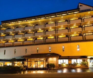 Evening exterior of Kawaguchiya Kinosaki Riverside Hotel showing lit balconies in Hyōgo, Japan