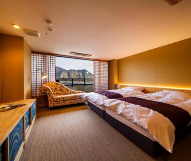 Twin beds, low wooden furnishings, shoji screens and window lounge at Kawaguchiya Kinosaki Riverside Hotel, Hyōgo