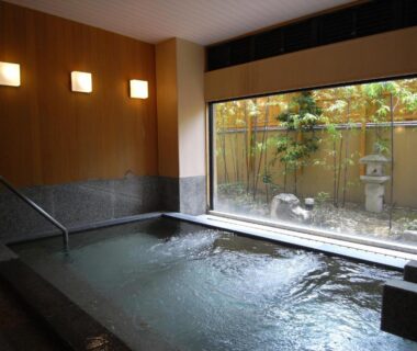 Indoor onsen bath with wooden walls, stone edge and garden view at Kawakamiya Kasuitei in Gifu