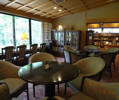 Ryokan lounge with round tables, upholstered chairs and large windows overlooking a garden at Kawakamiya Kasuitei Gifu