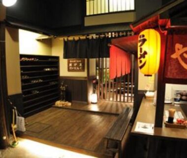 Traditional ryokan entrance with wooden genkan, shoe shelves, red noren curtains and lantern at Kawayu Kanko Hotel, Hokkaidō