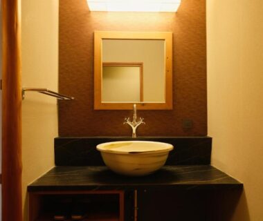 Ceramic sink on dark countertop with mirror and wooden accents at Keishokan Sazanamitei, Hiroshima