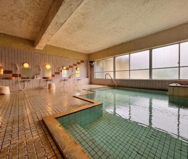 Tiled indoor onsen pool with shower stalls and stools at Kidoike Onsen Hotel Nagano