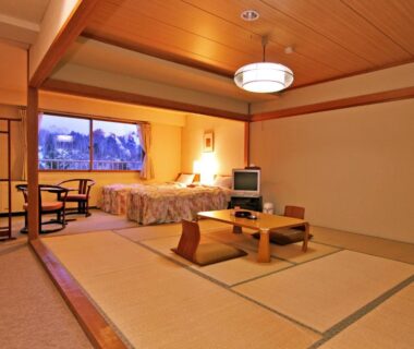 Spacious tatami room with low table, zabuton chairs, beds near window at Kidoike Onsen Hotel in Nagano