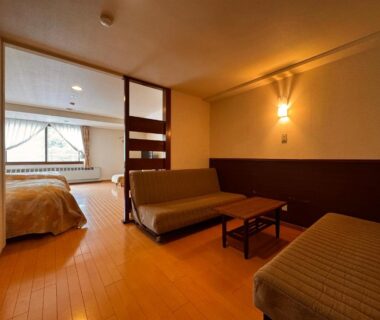 Warm wood-floored ryokan room with sofas, low table, sliding shoji partition and bed at Kidoike Onsen Hotel, Nagano