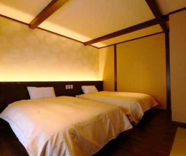 Twin beds in tatami-style ryokan room with warm lighting and wooden beams at Kii no Matsushima, Mie, Japan