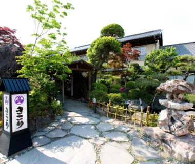 Stone path leading to a traditional ryokan entrance with manicured garden and signboard