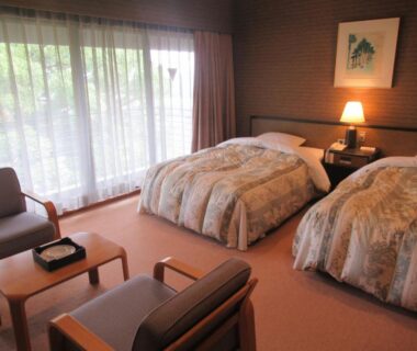 Quiet twin room with two beds, seating area and large curtained window at Kikuchi Kanko Hotel, Kumamoto
