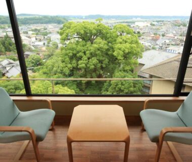 Two armchairs and small table by large window overlooking trees and town at Kikuchi Kanko Hotel, Kumamoto, Kyūshū