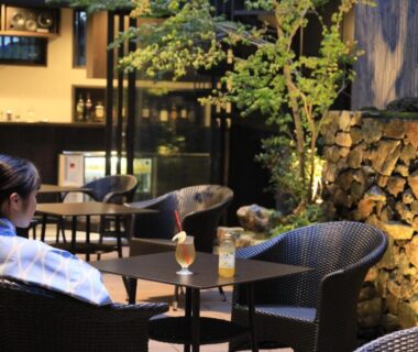 Guest in yukata seated on outdoor terrace with wicker chairs, small tables, drinks and a garden stone wall