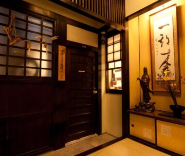 Warm-lit wooden ryokan entrance with shoji screens and calligraphy display at Kimi Ryokan Tokyo