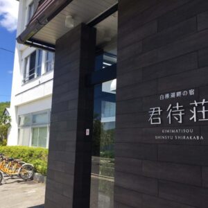 Building entrance with wooden signboard reading Kimimachisou and parked bicycles under blue sky in Nagano