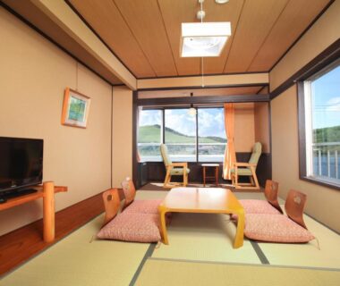 Tatami room with low table, floor cushions and wide window showing mountain view at Kimimachisou, Nagano